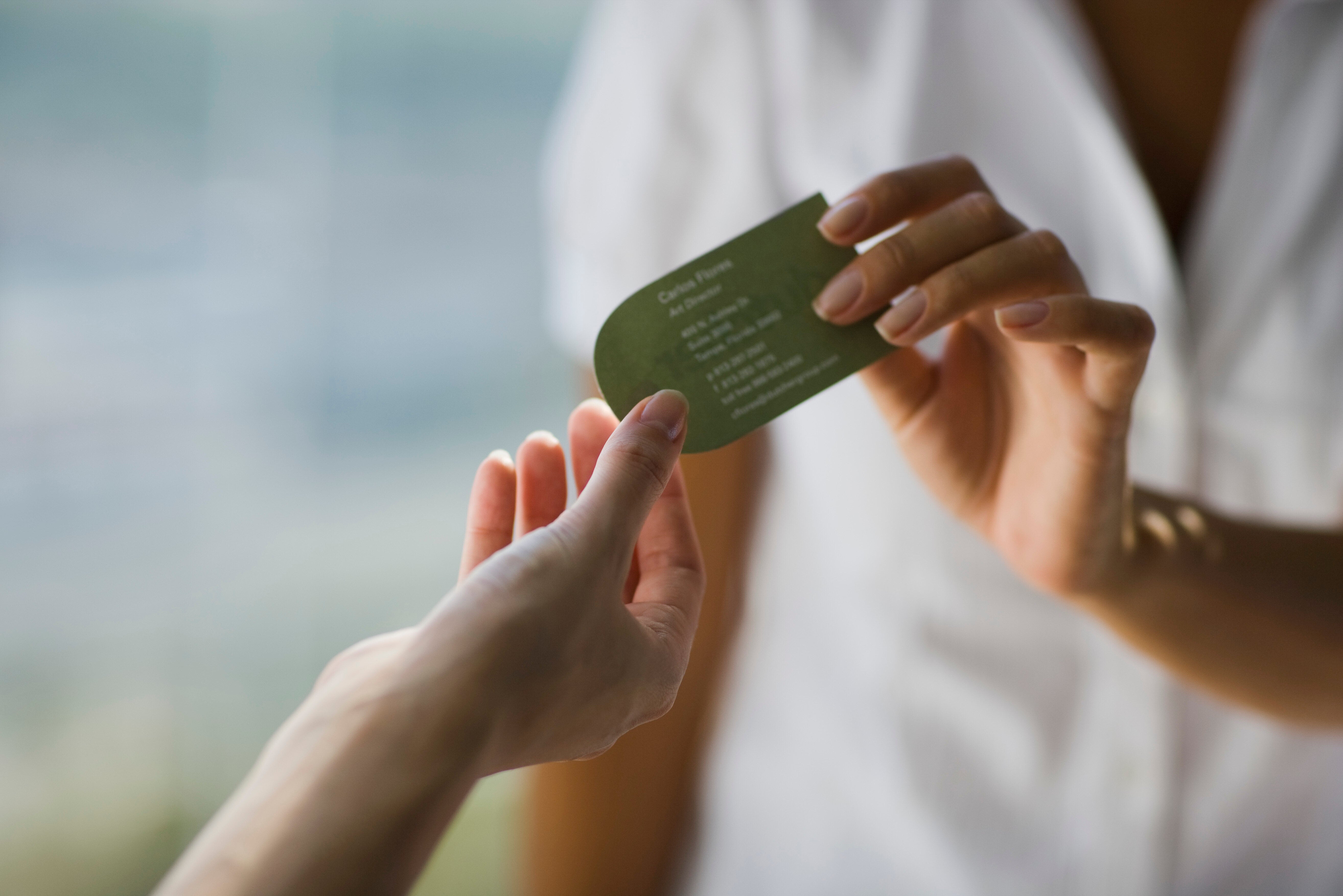 Person hands a business card to another person. Card details are not visible