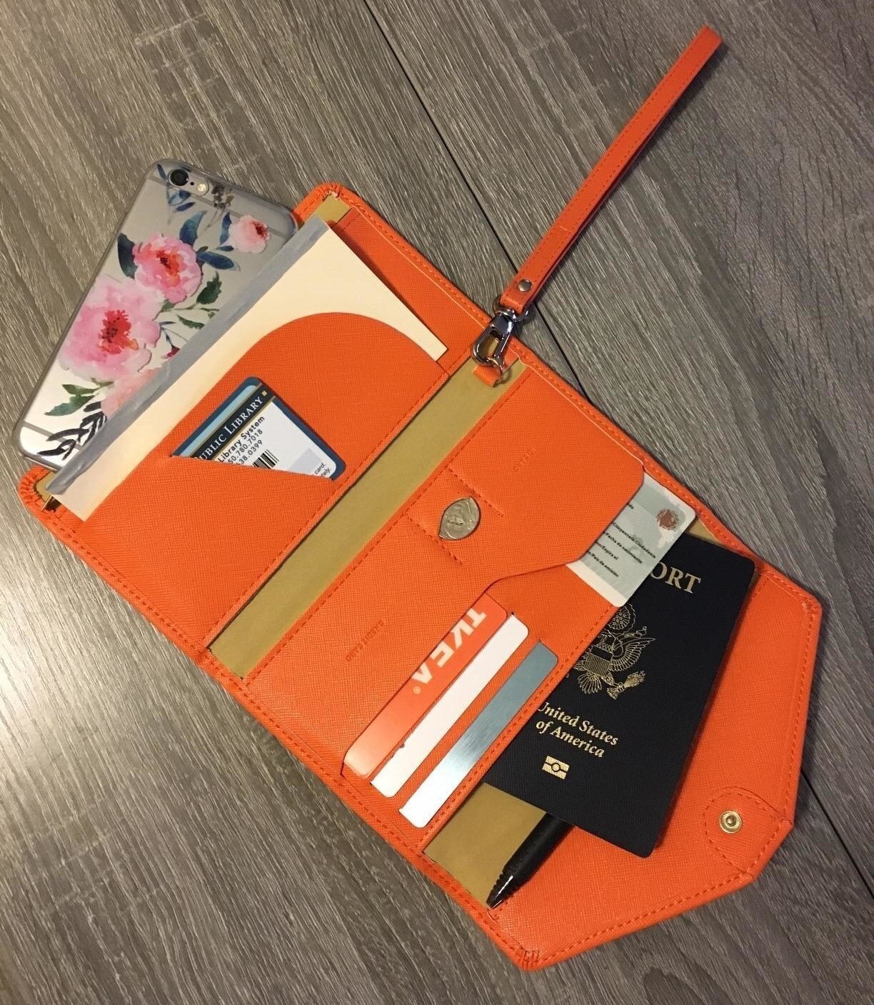 Open orangish question wallet with phone, cards, pen, and passport connected a woody surface