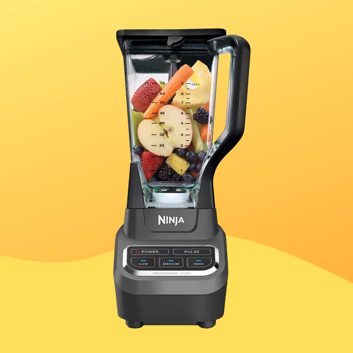 Ninja blender filled with assorted fruits including strawberries, bananas, and berries, placed against a gradient background