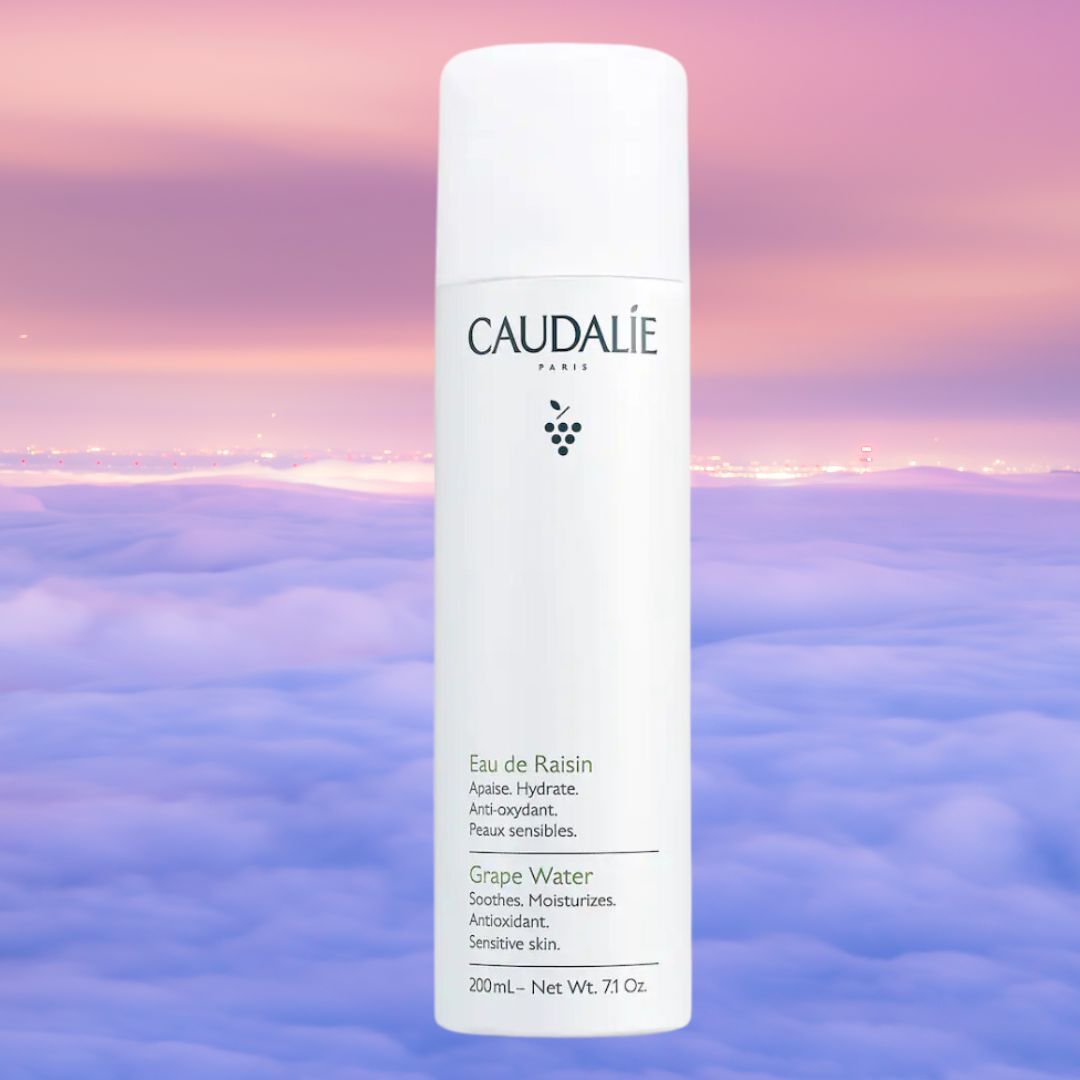 Caudalie Paris Grape Water bottle on a dreamy, cloud-filled background. Text indicates it soothes, moisturizes, is antioxidant-rich, and suitable for sensitive skin