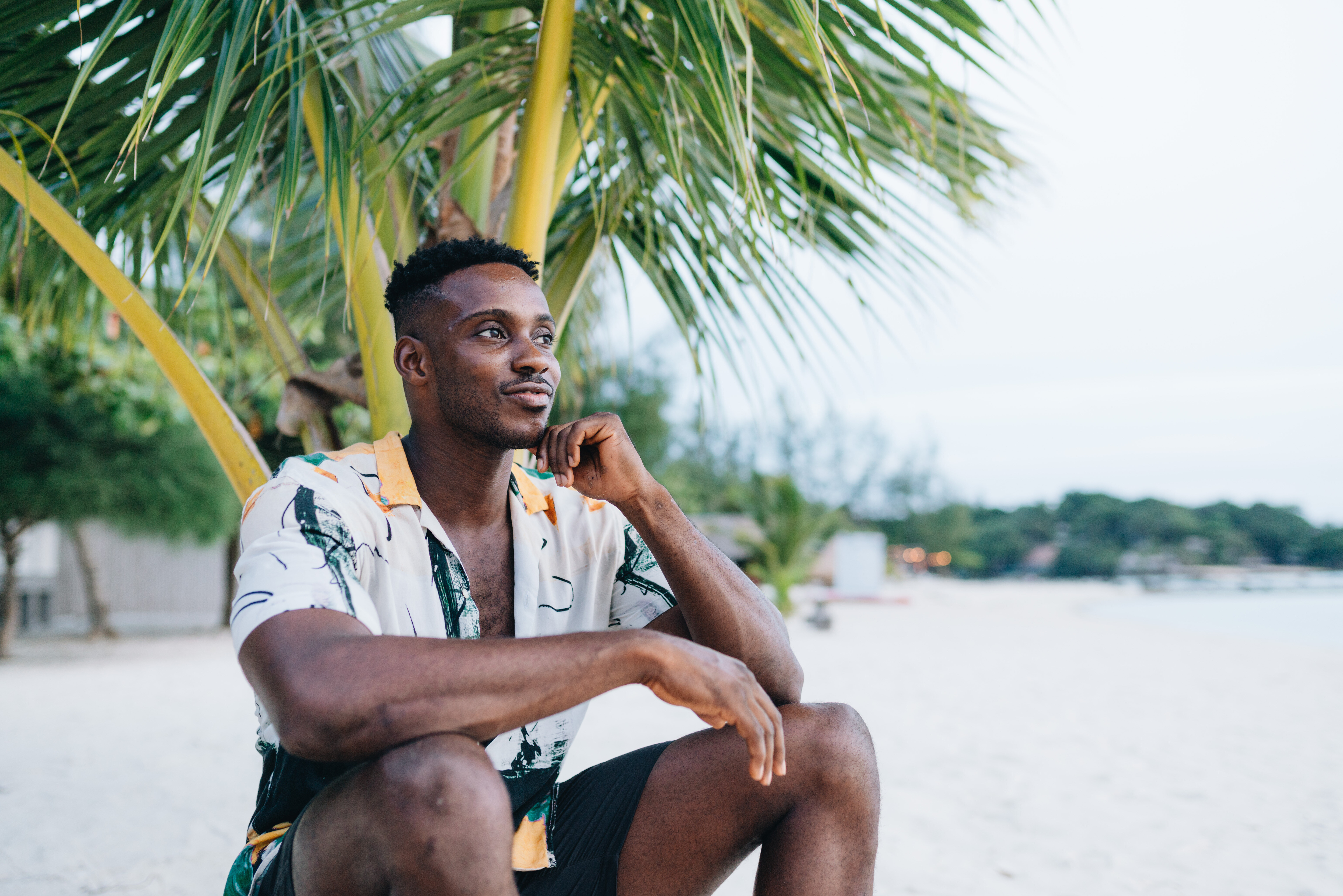 man relaxing underneath a palm tree at the beach