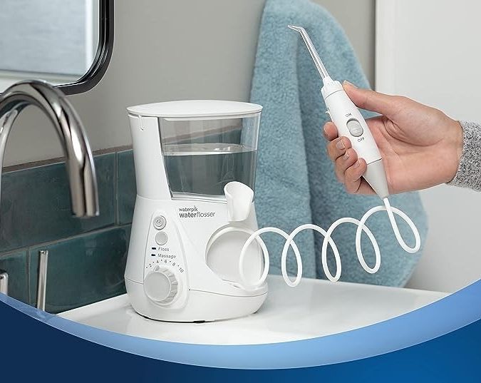 Person holding a water flosser next to its base station on a bathroom counter