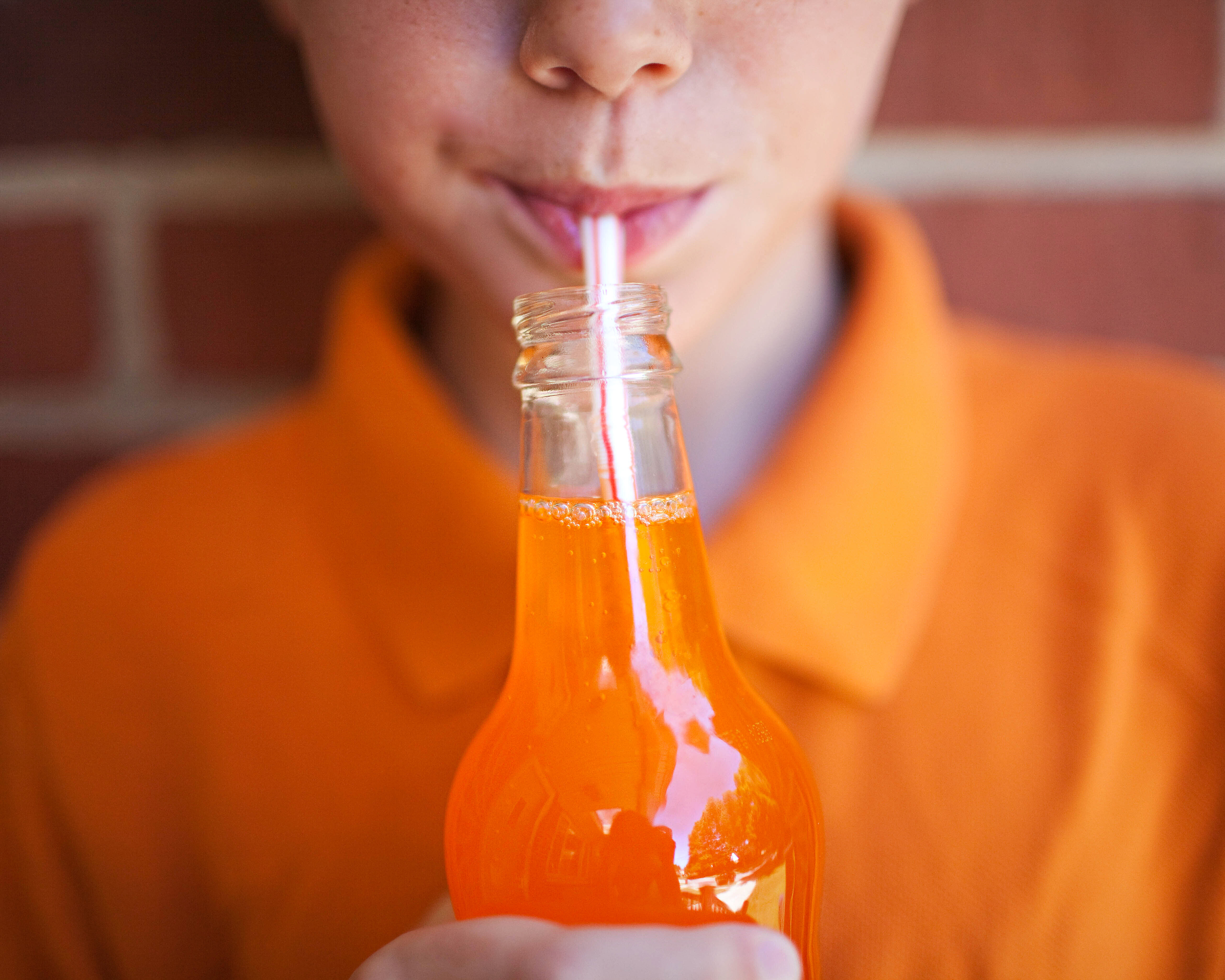 Person sipping a beverage from a glass bottle using a straw