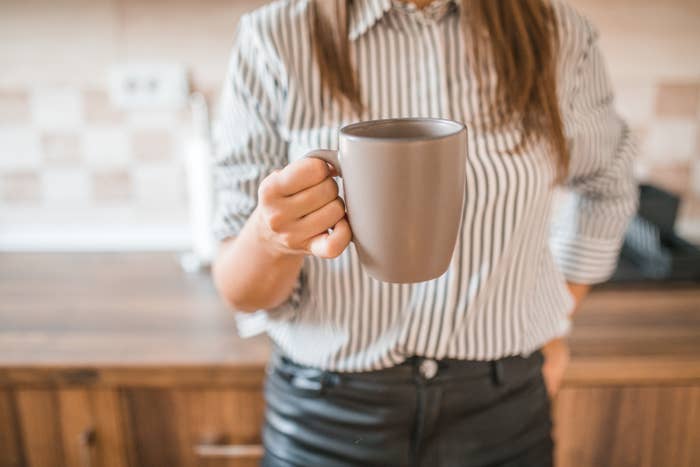 A person in a striped shirt holds a ceramic mug in a kitchen. Their face is not visible