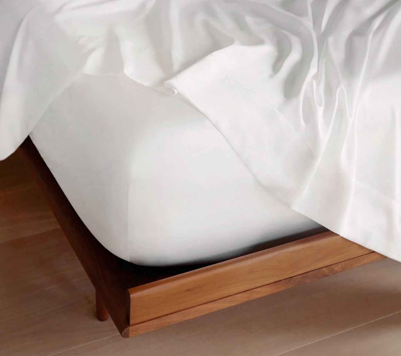 An unadorned white fitted sheet on a bed with a visible wooden bed frame