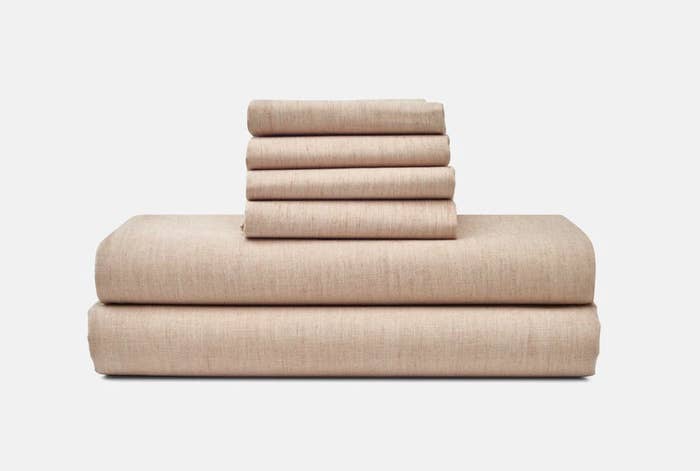 Three neatly stacked sets of folded beige bed linens on a white background