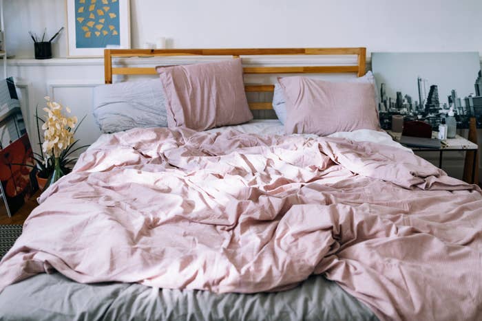 Unmade bed with crumpled pink duvet, pillows, and a cityscape wall art, suggesting cozy bedding products for sale