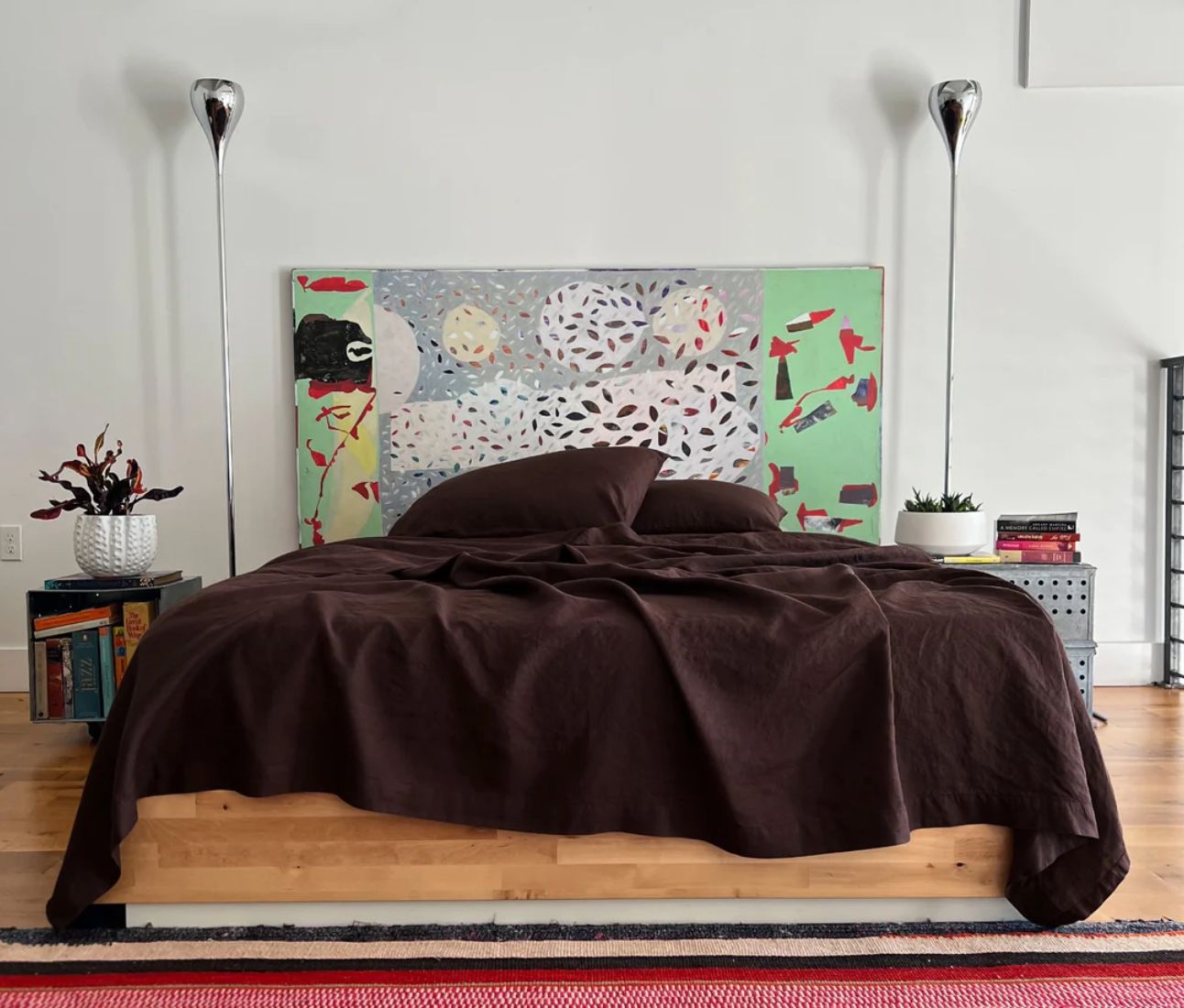 Bedroom with a large abstract painting above the bed, featuring a brown duvet cover and decorative floor lamps on either side