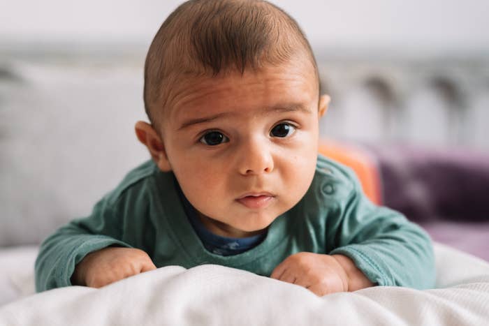 A baby with a concerned expression is lying on their stomach, looking up