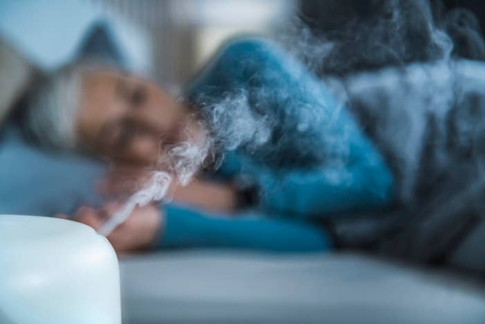 A humidifer blowing out air next to a woman sleeping.
