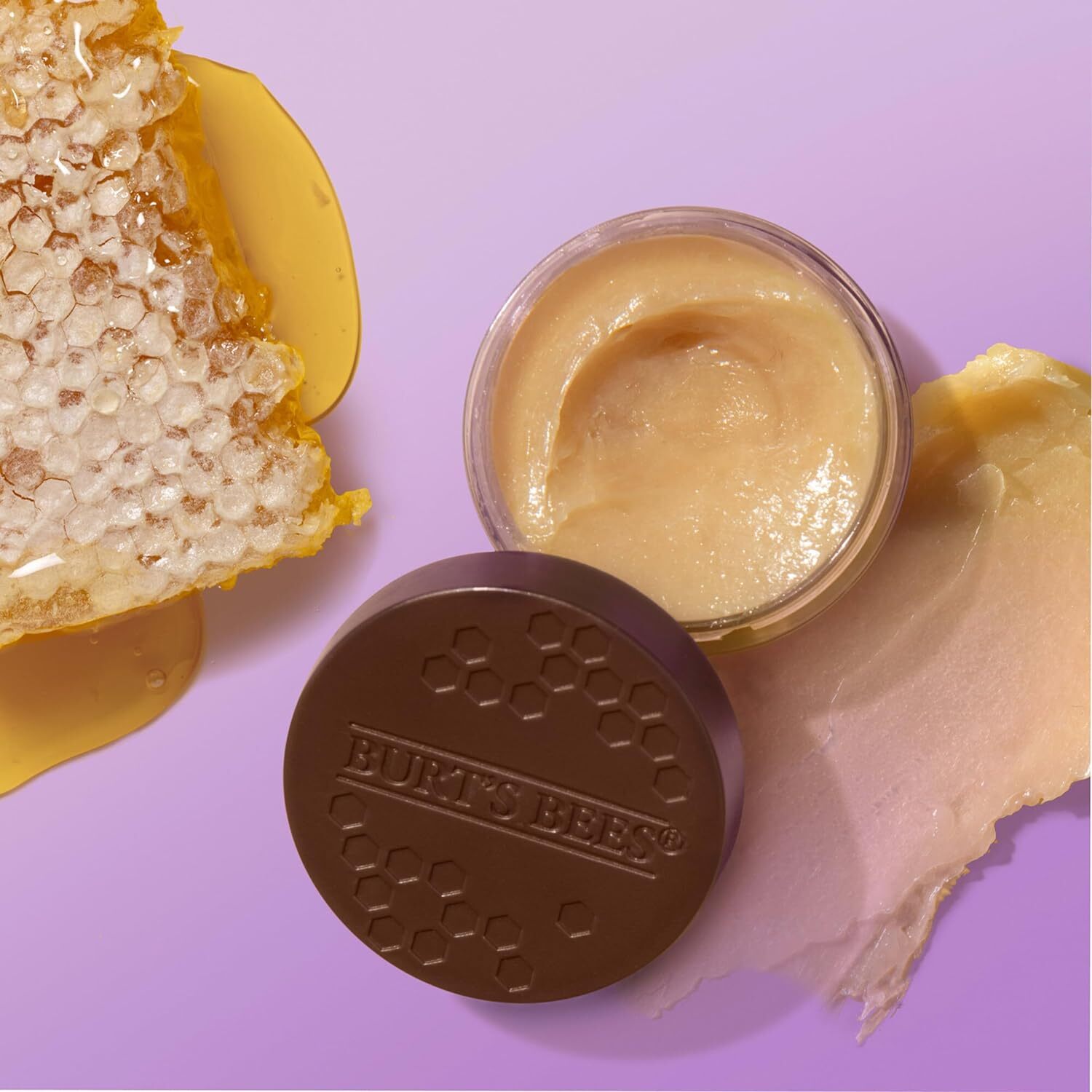 Open jar of Burt&#x27;s Bees cream with honeycomb and lid nearby, suggesting natural ingredients in a product showcase