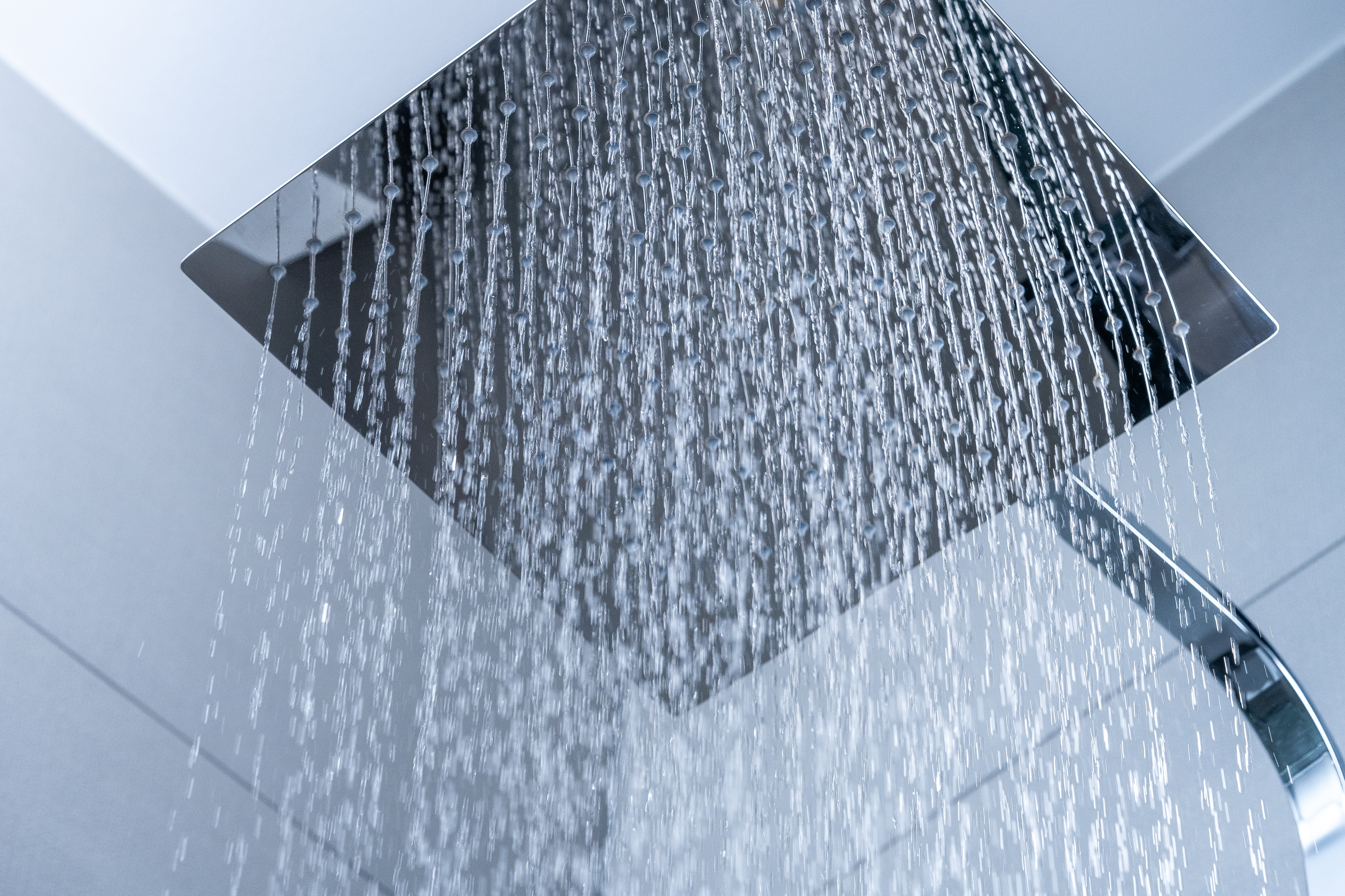 Water flowing from a square shower head against a blurred background