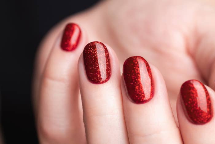 Close-up of a person&#x27;s hand with shimmering red nail polish, suggesting a glam look for shoppers