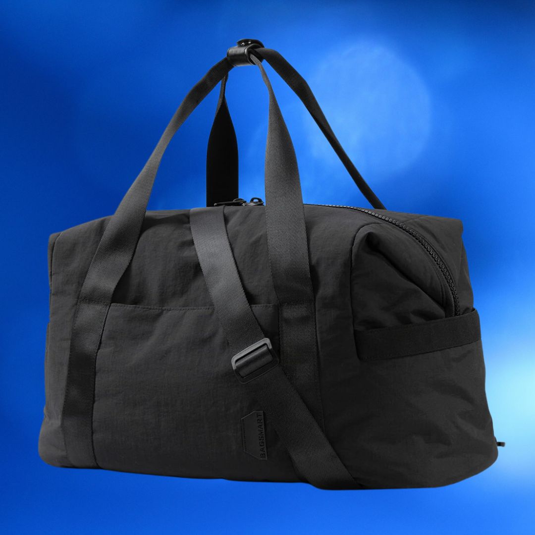 Black duffle bag with shoulder strap and side pocket, floating against a blue backdrop