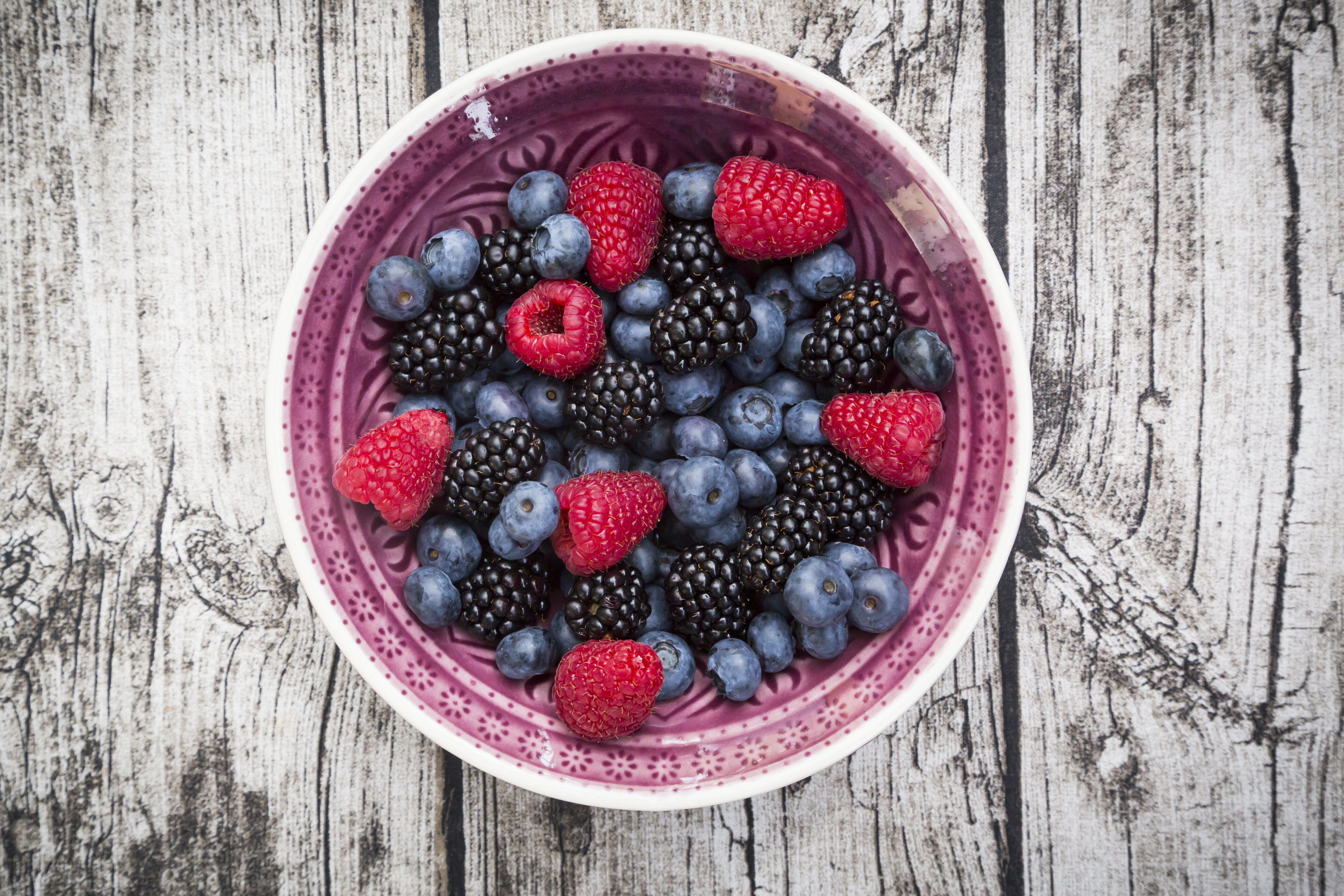 A bowl of mixed berries including raspberries, blueberries, and blackberries on a wooden surface