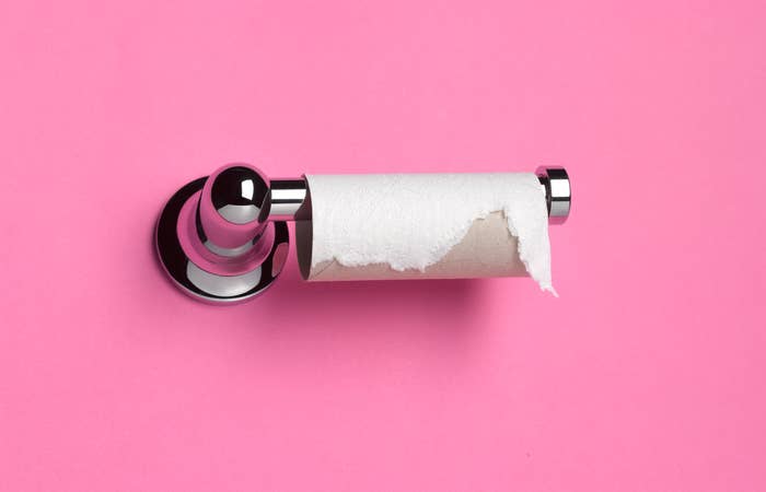 Empty toilet paper roll on a holder against a pink background, signifying the need for a refill