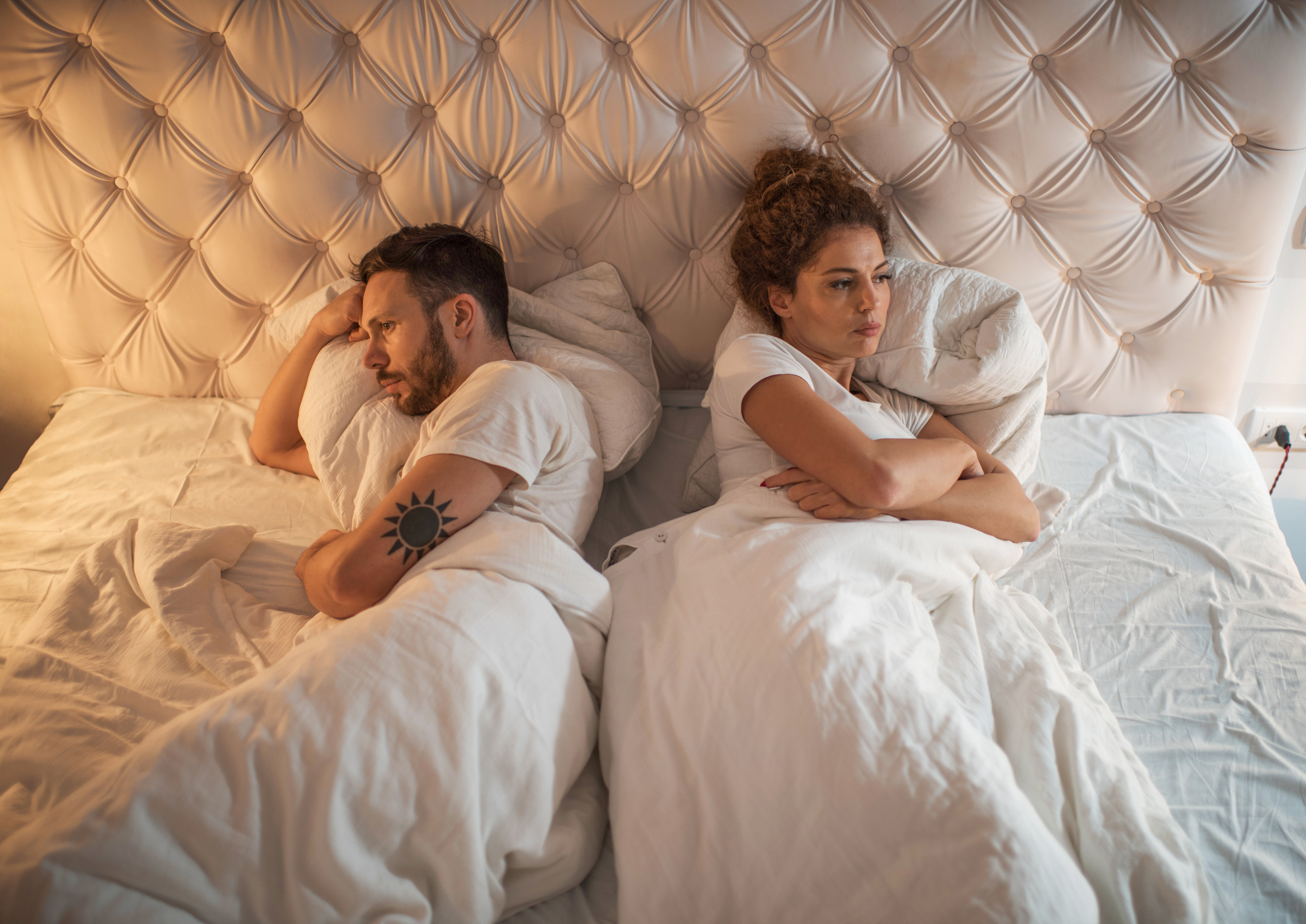 Two people lying in bed facing away from each other, appearing upset or in disagreement