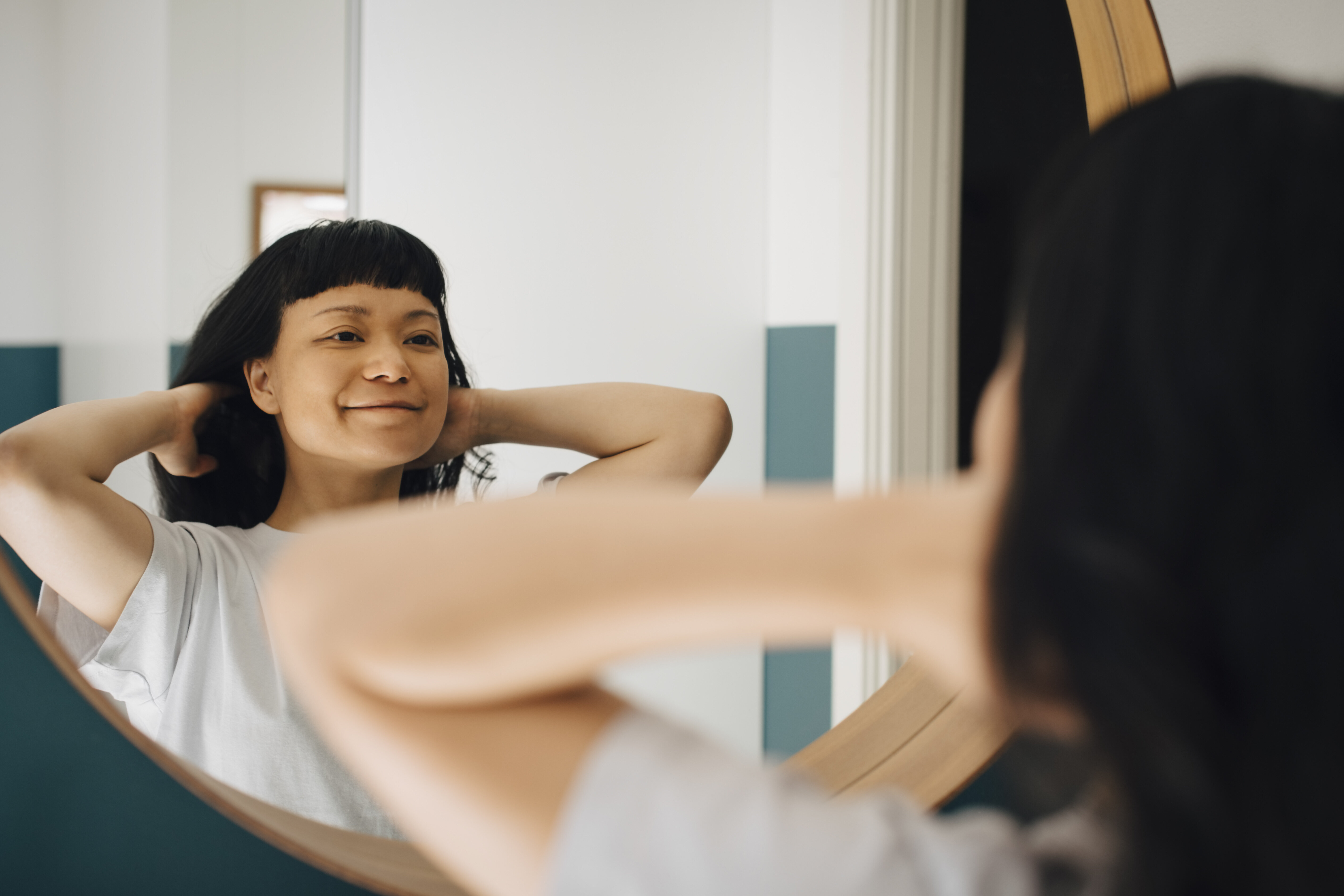 Person smiling at their reflection in a mirror, hands behind head, promoting self-love and positivity
