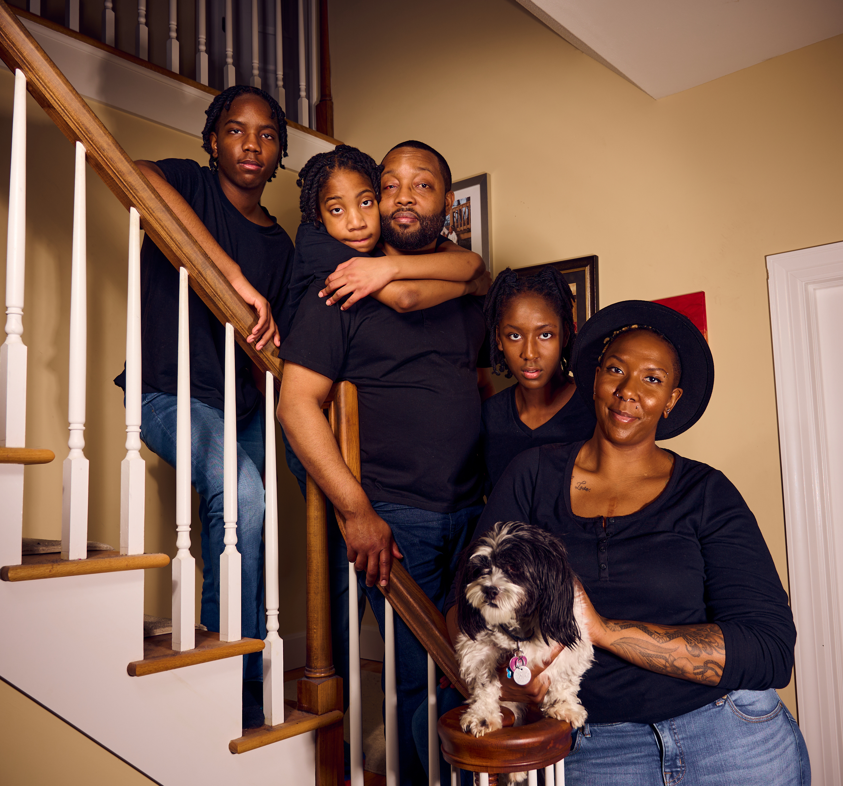 Family with two adults, three children, and a dog posing on staircase, looking at the camera, showing togetherness