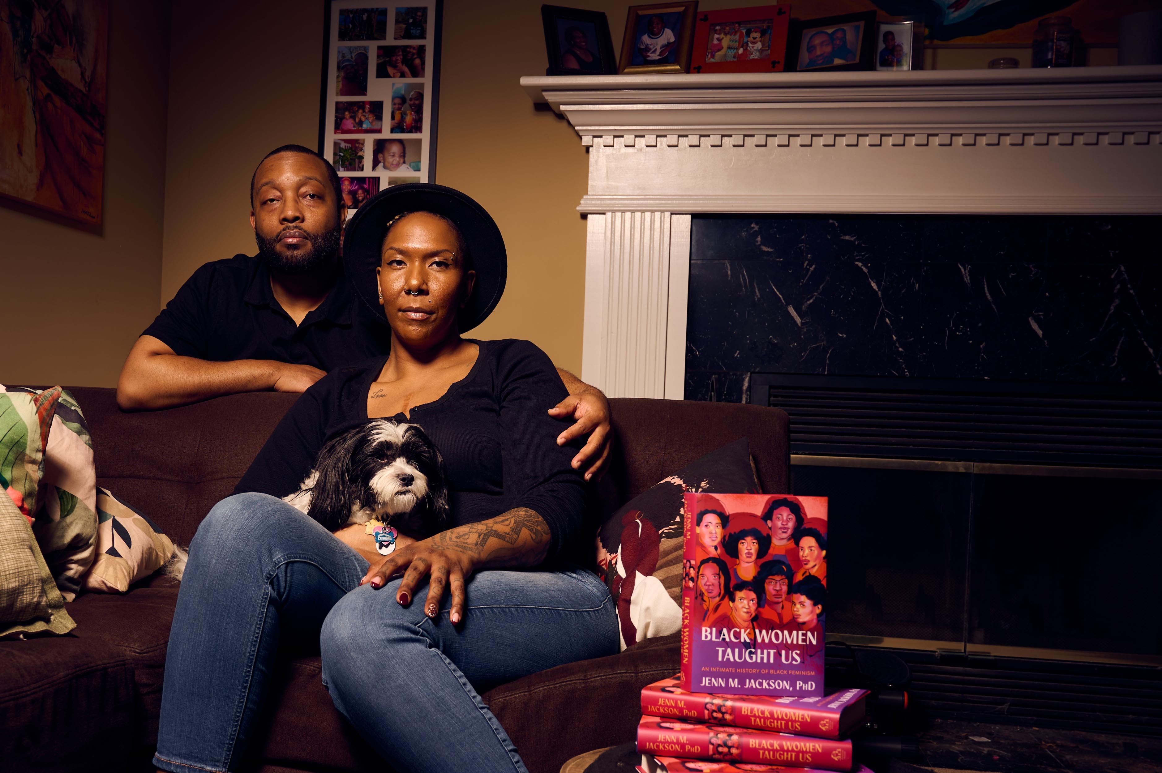 Couple sitting on a couch with a dog and a stack of books including &quot;Black Women Taught Us&quot; by Jewell Jackson