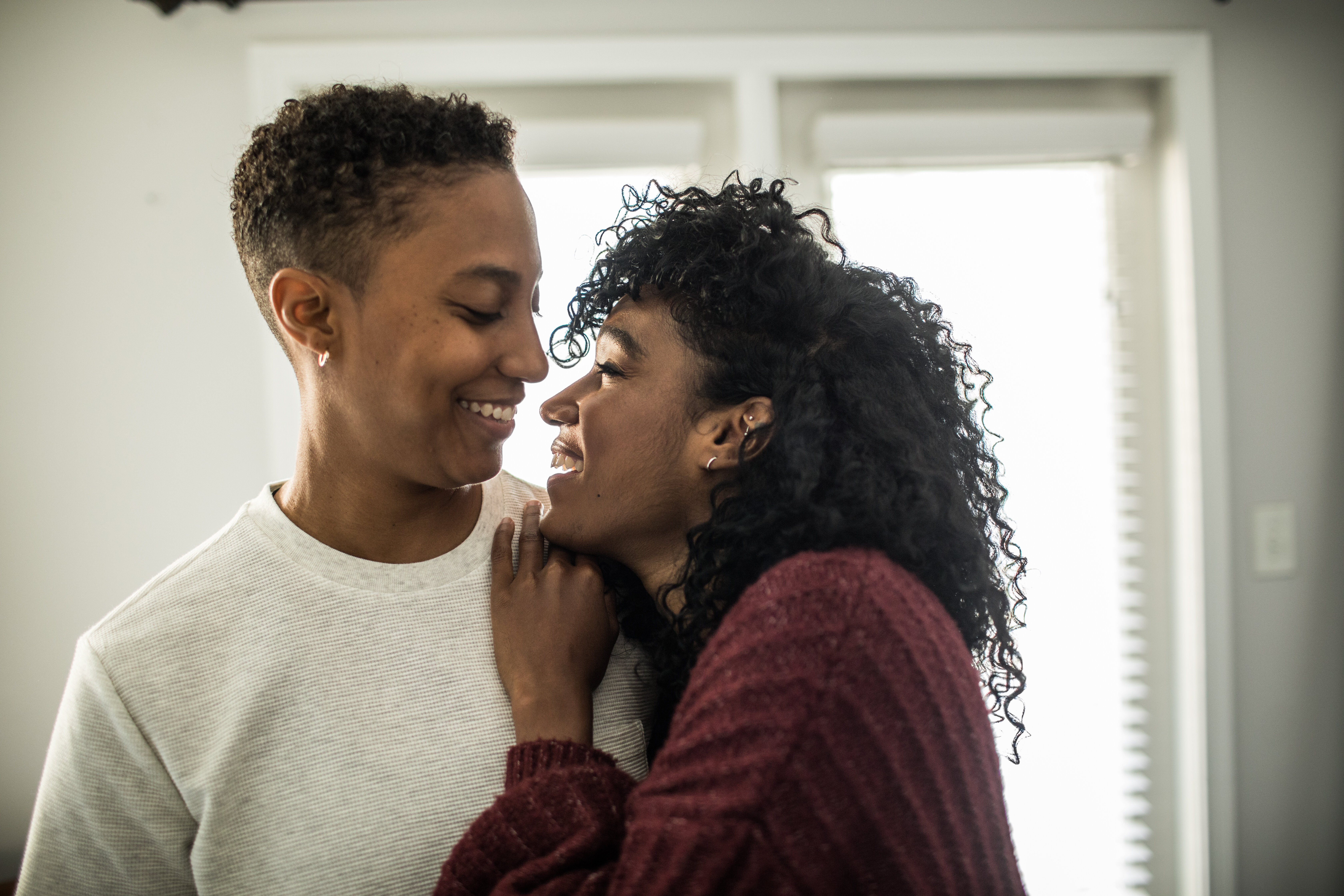 Two people smiling at each other, close-up, one with short hair and the other with curly hair
