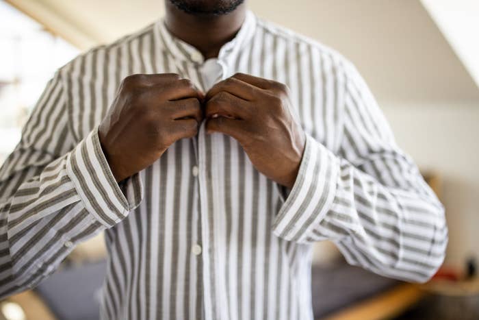Man buttoning his striped shirt, focused on hands and shirt details