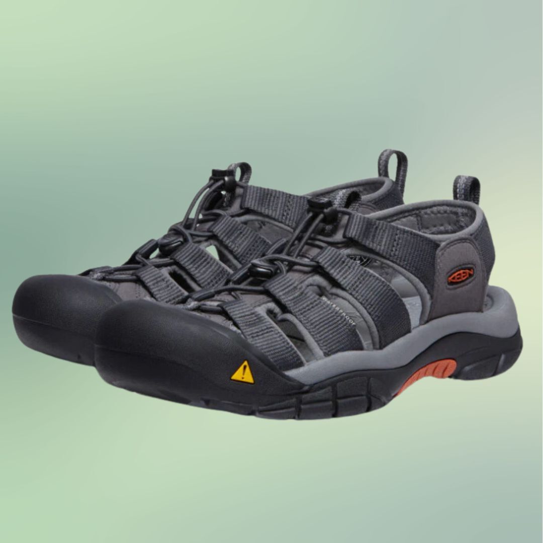 A pair of sporty, black trail shoes with laces and an orange and black sole on a gradient background