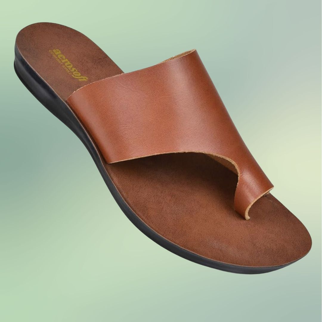 A single brown leather sandal with a wide strap and flat sole against a green background