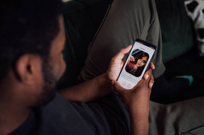 Person viewing a dating profile on a smartphone. The profile shows a woman&#x27;s photo and interface elements