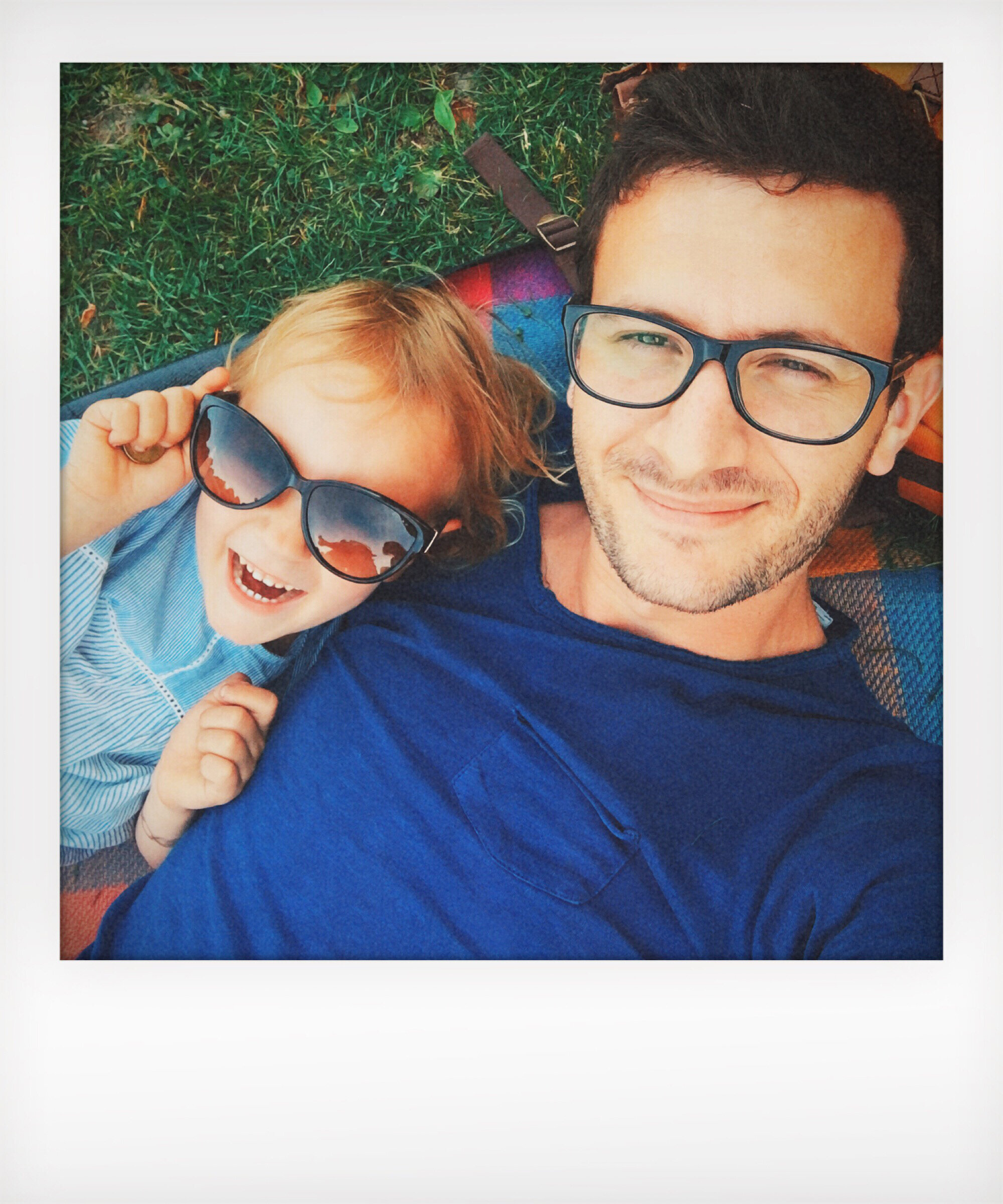 Man and child laying on grass, smiling at the camera, child wearing sunglasses