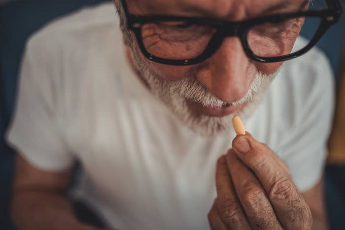 Elderly man with glasses and beard looking closely at a small object in his hand