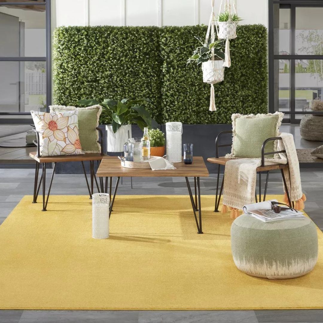 A bright yellow rug on a deck with midcentury modern-style outdoor furniture