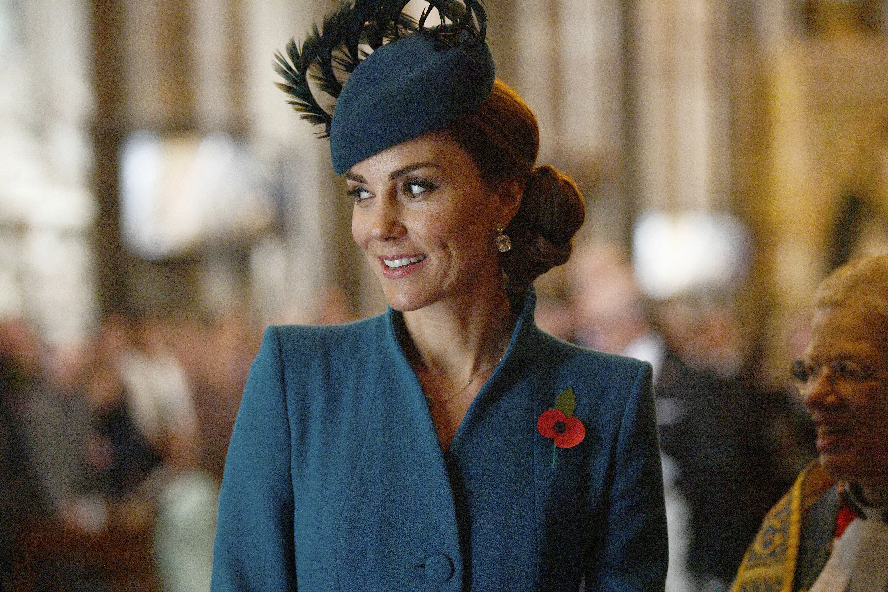 Kate Middleton in teal coat and fascinator with a poppy pin, attending a formal event