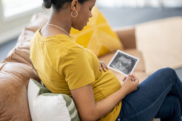 Pregnant person sitting, holding and looking at a sonogram picture