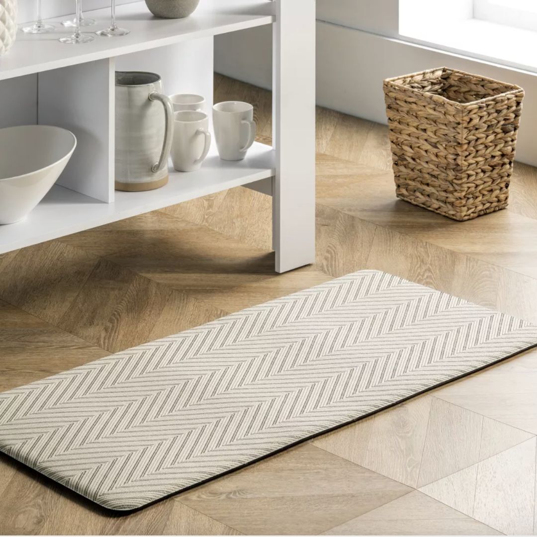 A chevron pattern anti-fatigue mat in neutral colors on a wood floor