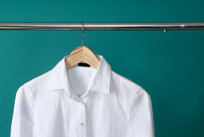 White shirt hanging on a hanger against a teal background