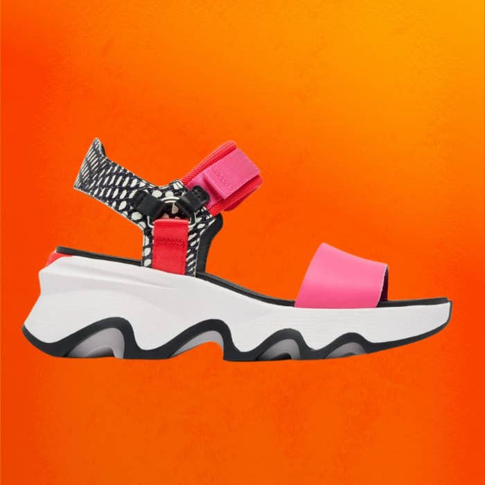 The Sorel Kinetic Impact Y-Strap sandals against an orange background