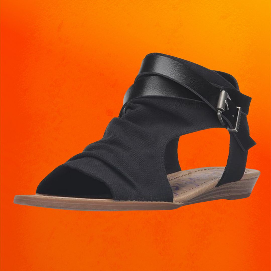 Black suede wedge sandals against an orange background