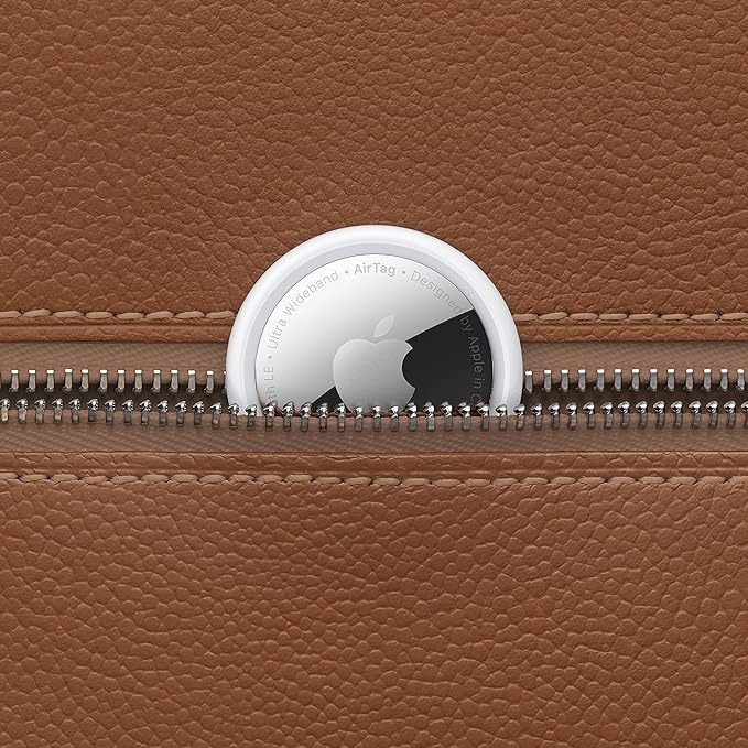 Apple AirTag positioned on a brown leather surface with a zipper surrounding it