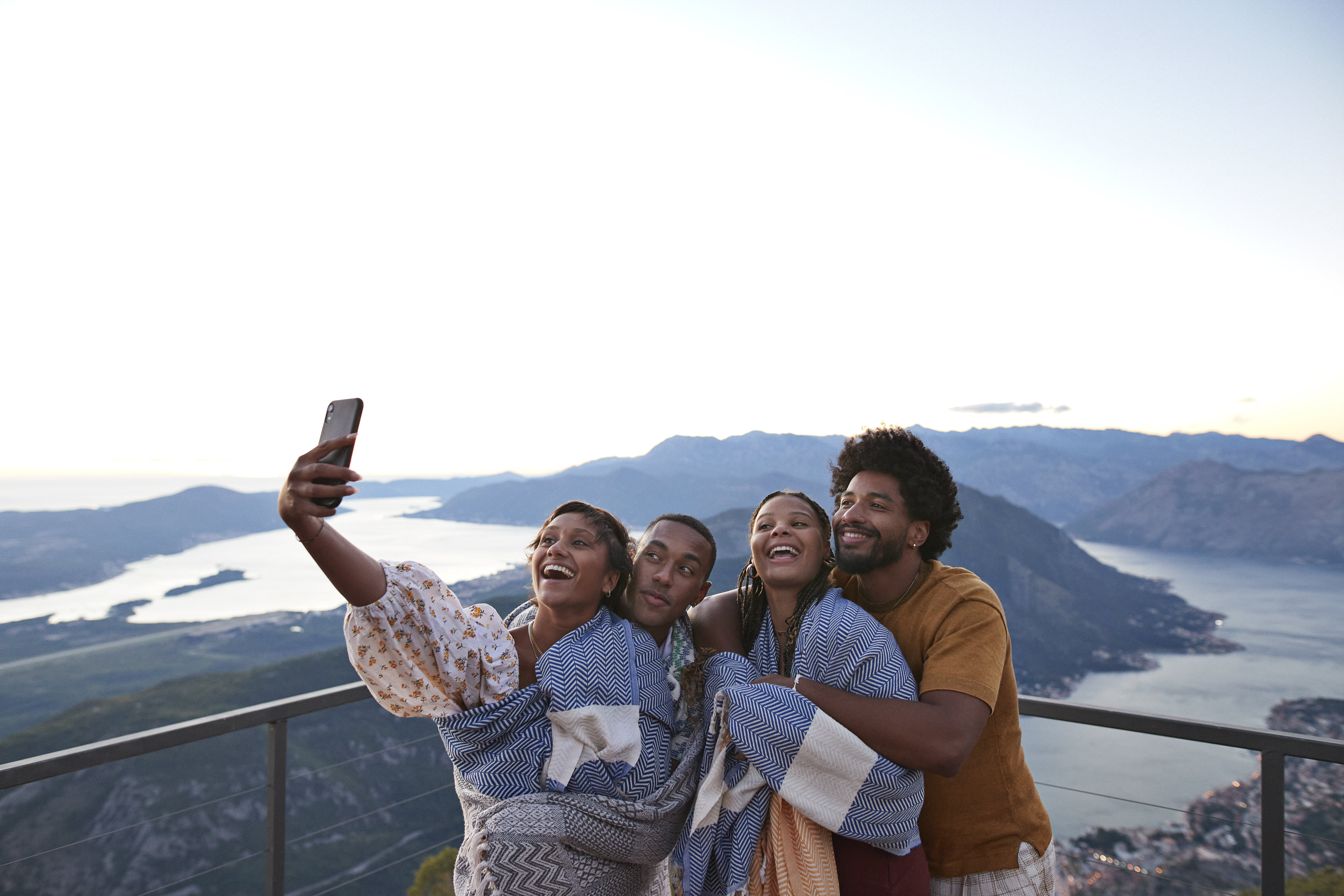 Four friends taking a selfie with a scenic mountainous backdrop during travel