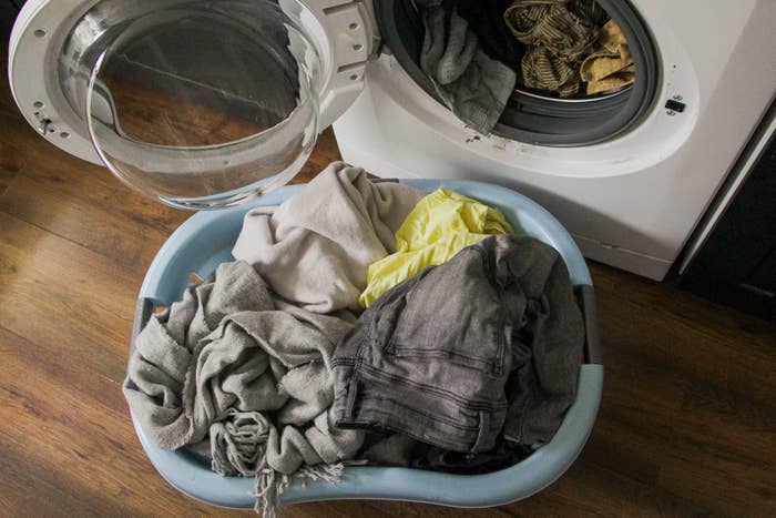 A laundry basket with clothes in front of an open washing machine