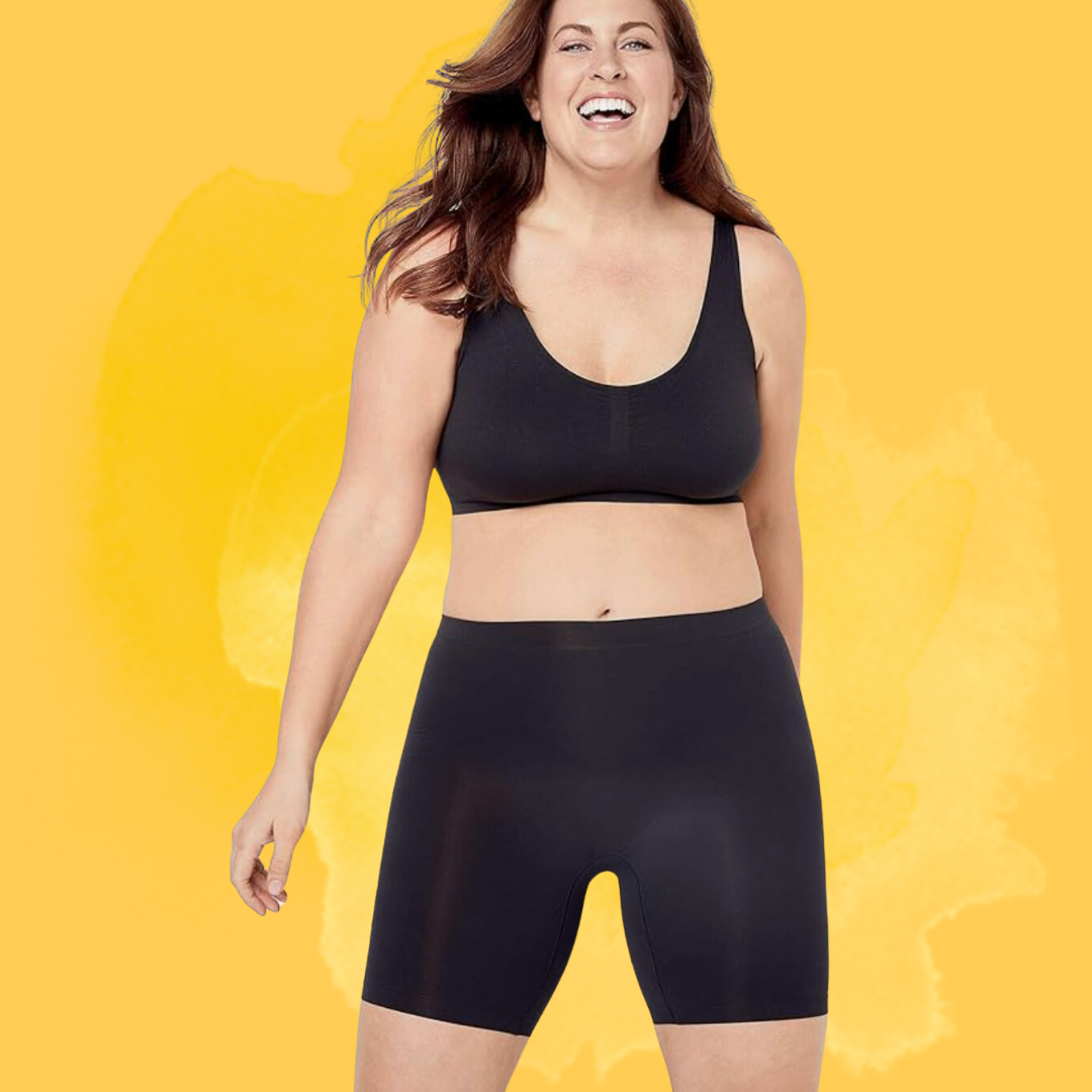 Person smiling and wearing a achromatic sports bra with matching biker shorts, lasting against a plain background