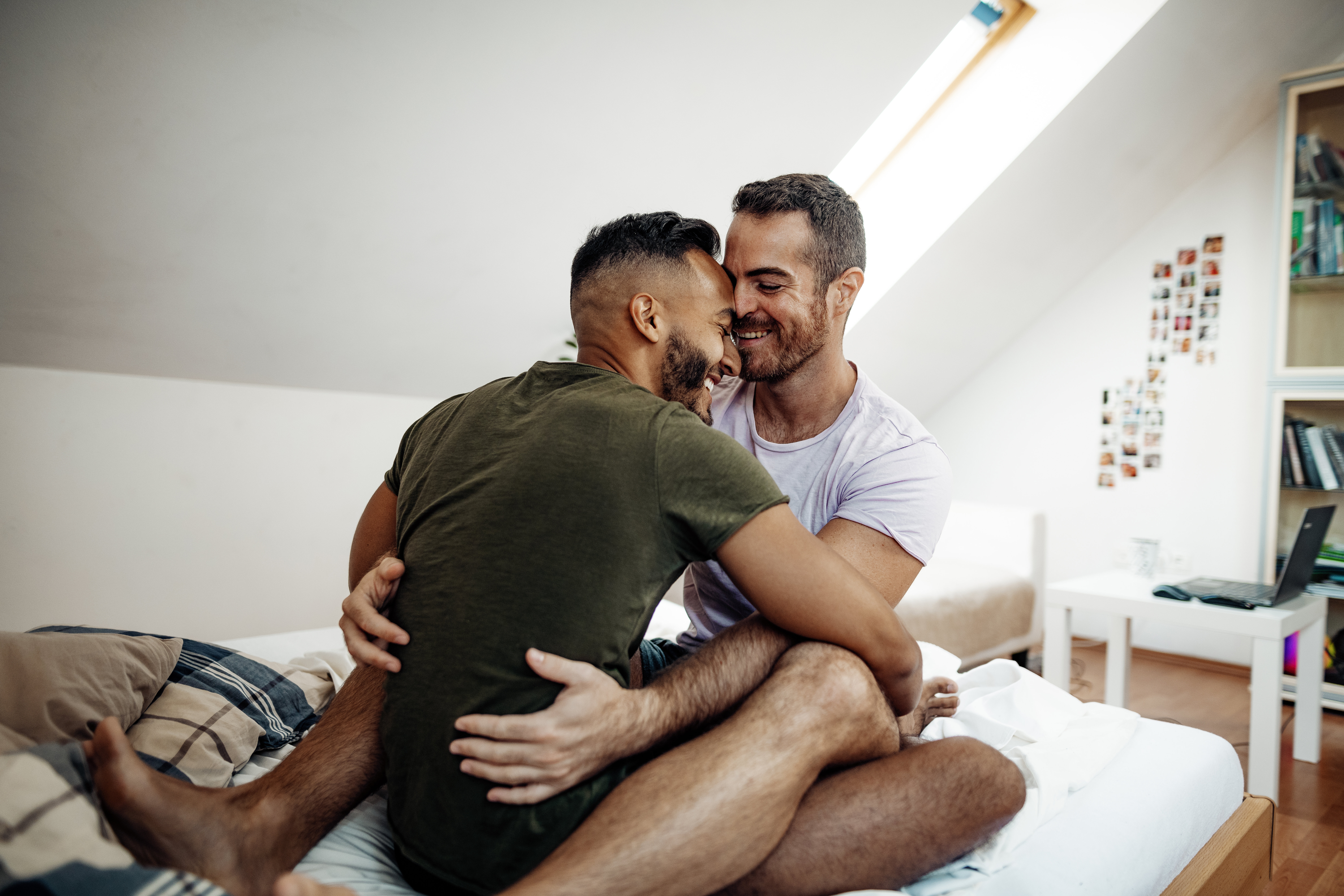 Two men embracing and smiling on a bed in a cozy room setting