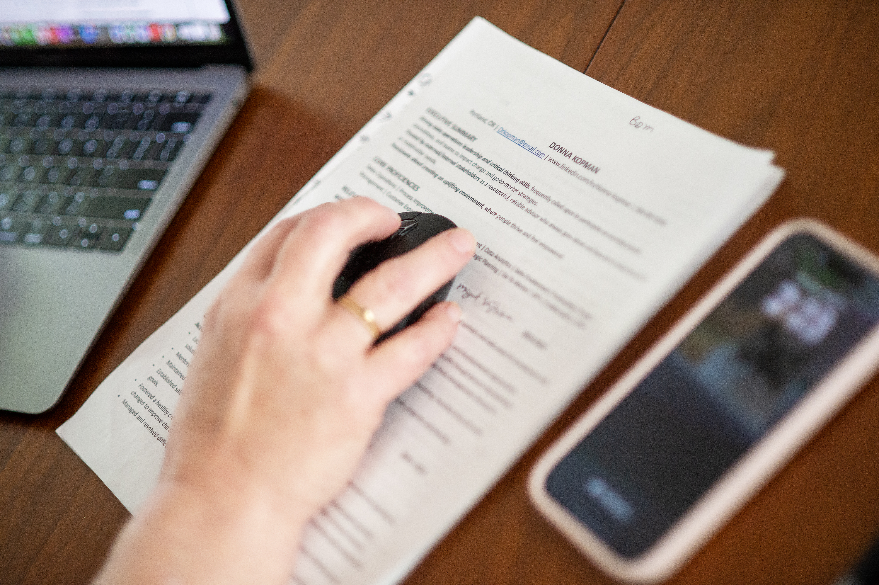 A hand using a mouse over documents next to a laptop and a smartphone