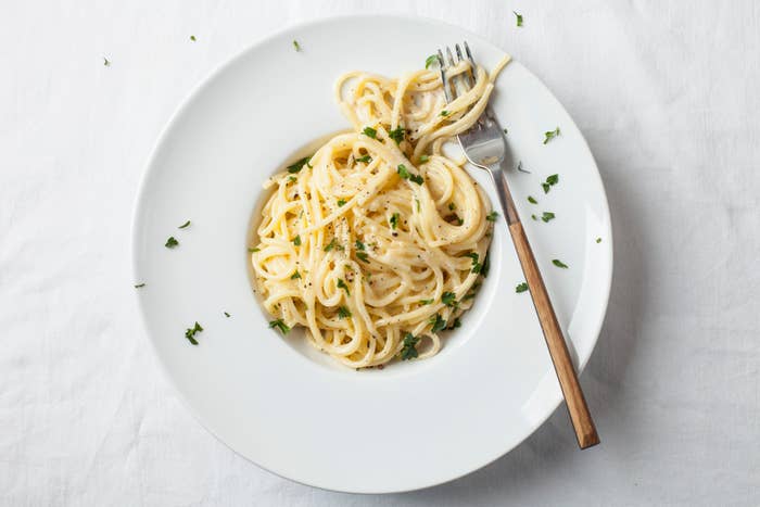 A plate of spaghetti with creamy white sauce, garnished with chopped parsley, and a fork resting on the plate