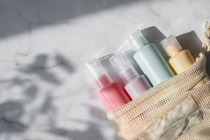 Four skincare bottles in a beige mesh bag on a white marble surface with shadows