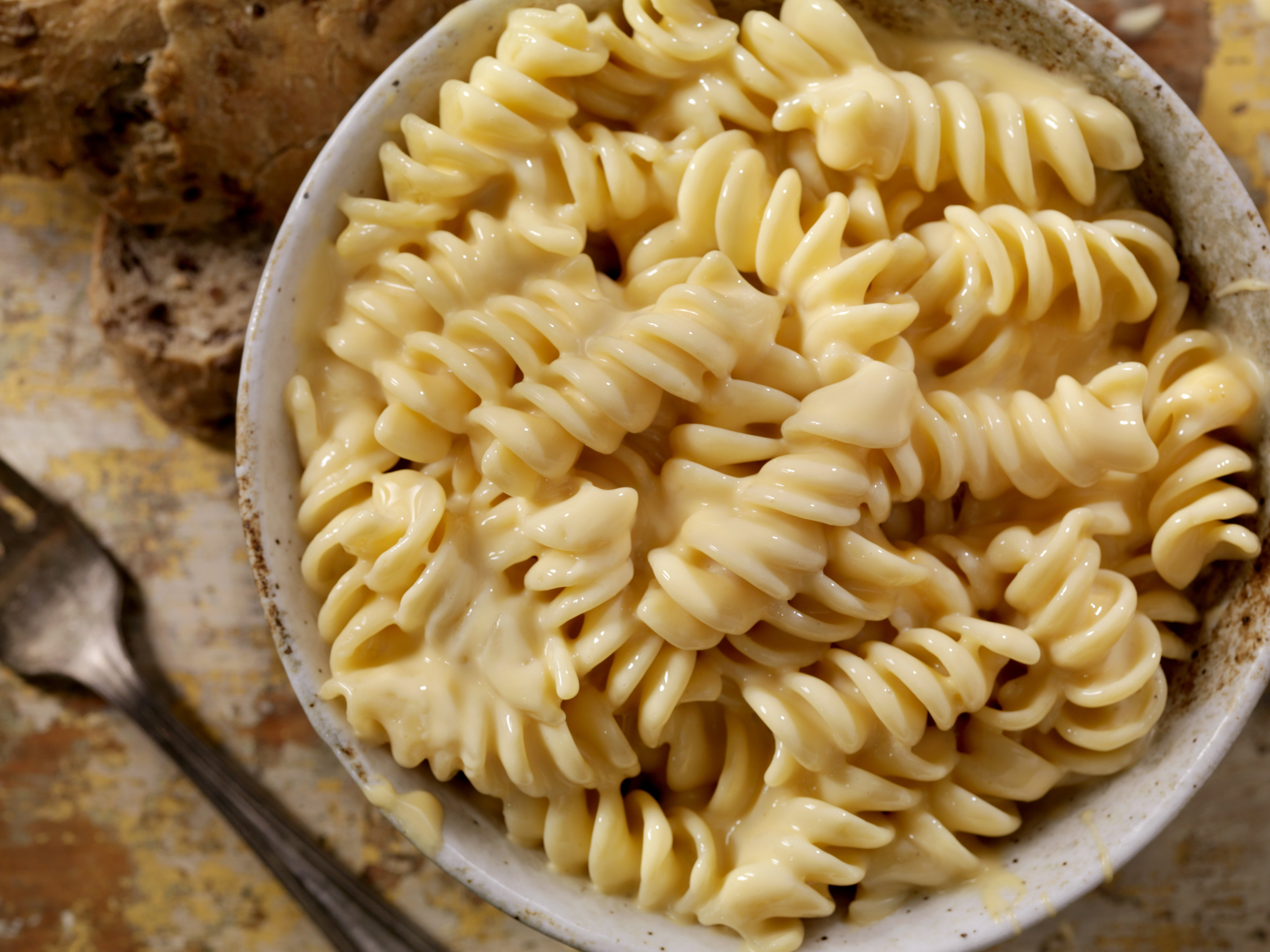 Close-up of a bowl of creamy macaroni and cheese with a fork and bread in the background