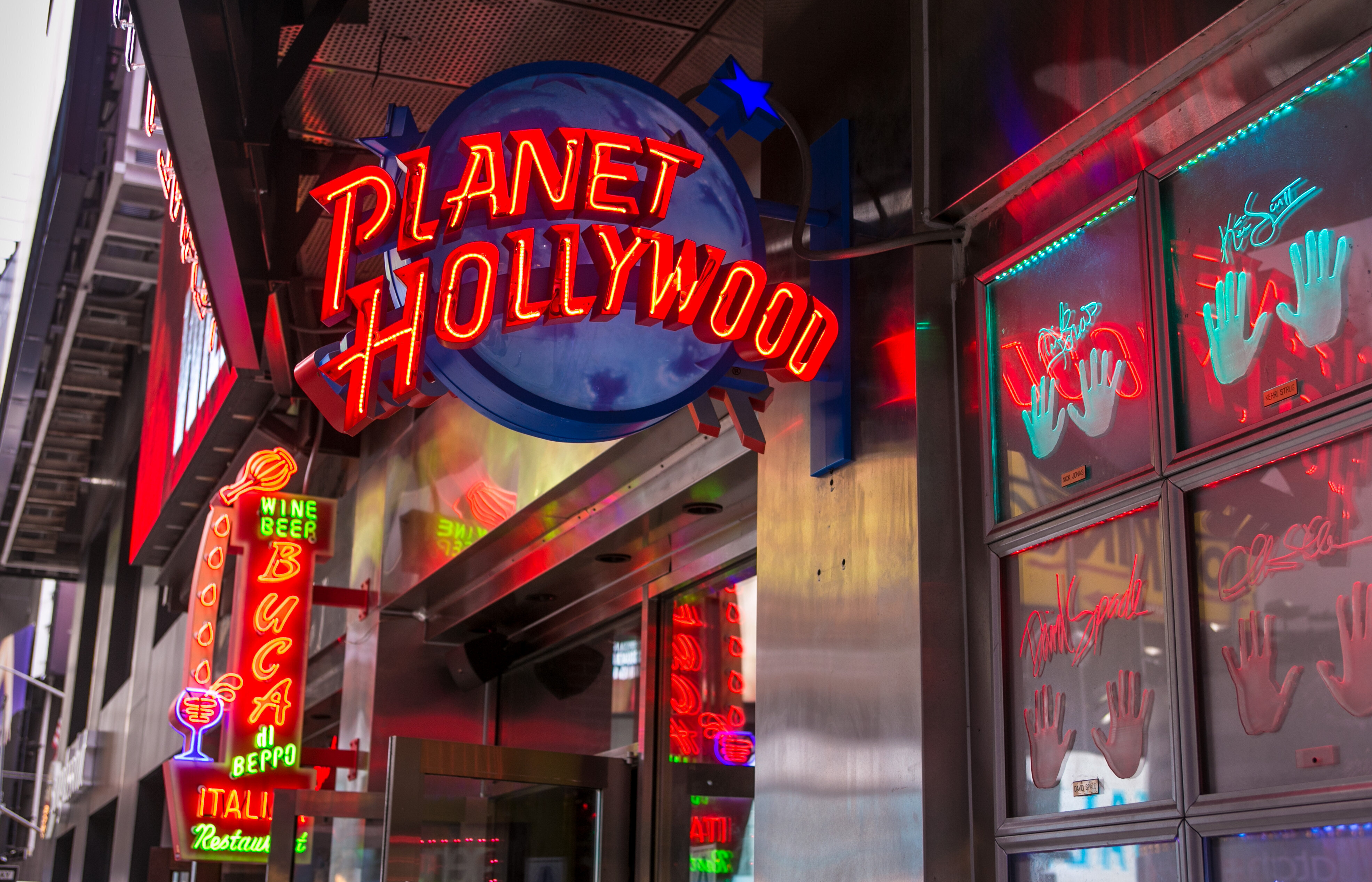Bright neon signs outside Planet Hollywood and nearby establishments, featuring vivid handprints and text, creating a vibrant nightlife ambiance