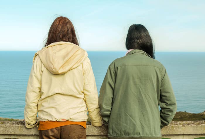 Two people stand with their backs to the camera, looking out over the ocean