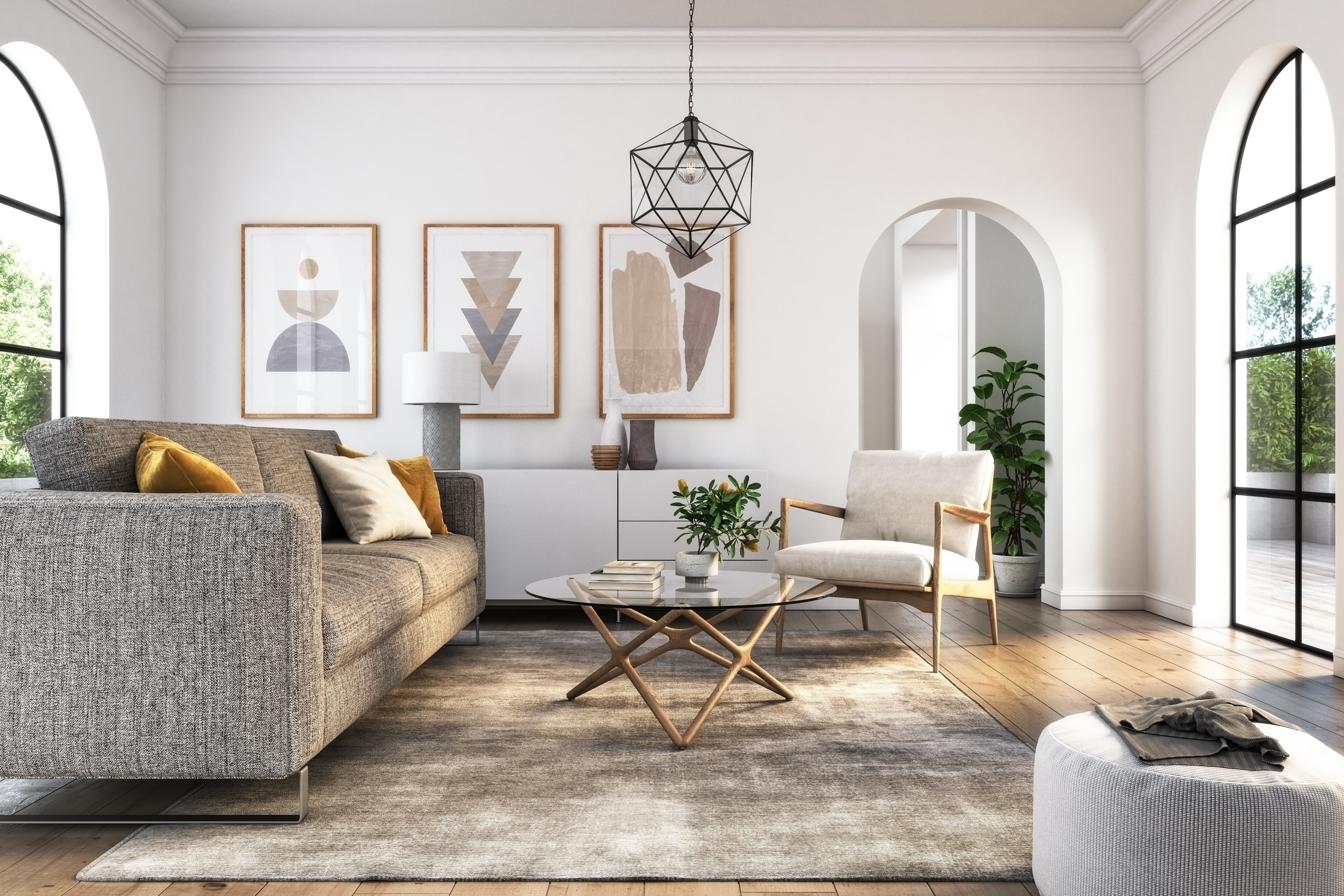 A bright, modern living room with a gray sofa, white armchair, glass coffee table, and wall art. Large windows, arched doorway, and potted plants add to the decor